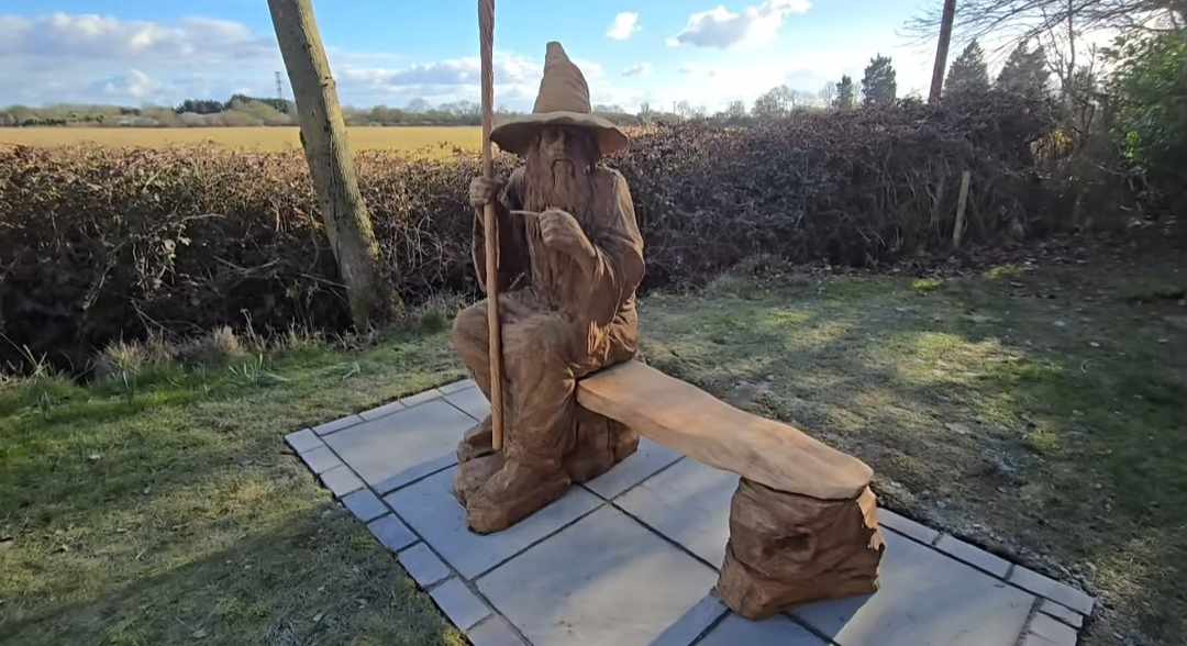 a wooden sculpture of Gandalf sitting on a bench in a garden